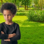 Angry little boy with arms folded, wearing black shirt. Blurred playground background. How to Discipline Your Child